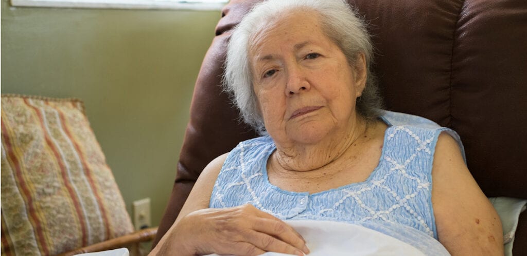 Elderly woman resting thoughtfully on a couch.