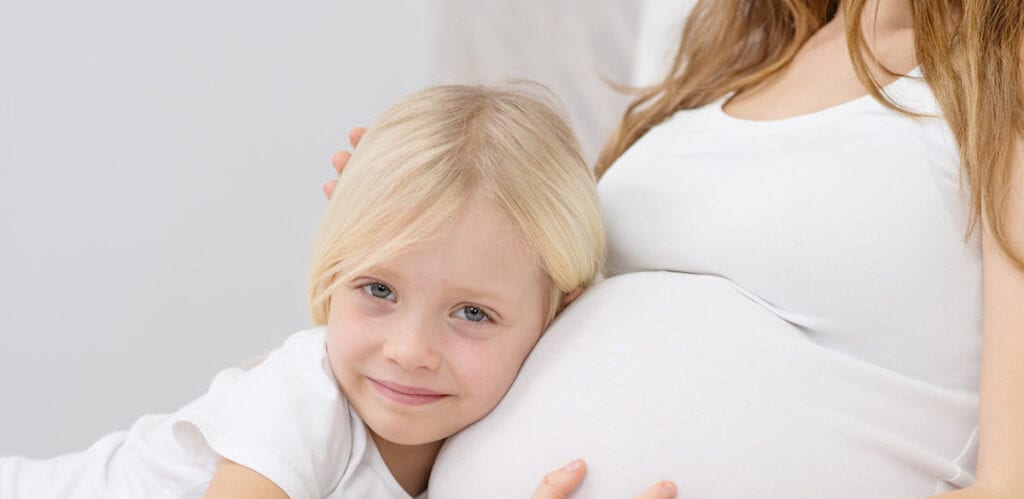 A little girl gently resting her head on a pregnant woman's belly.